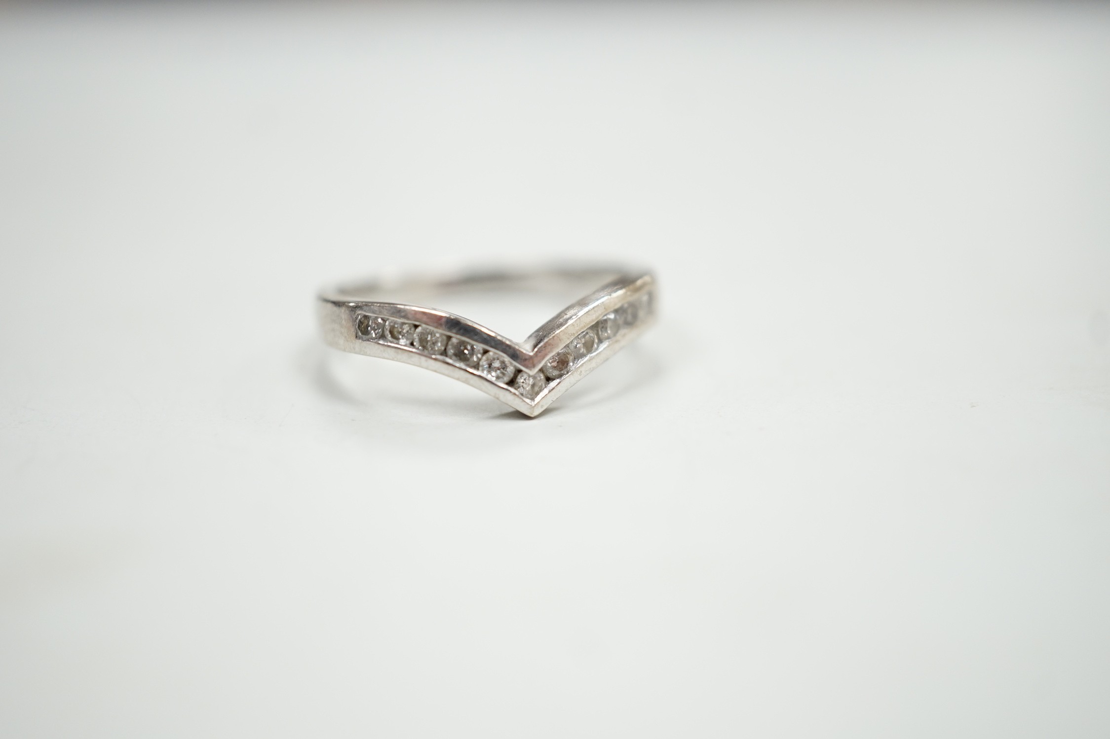 A modern 18ct white gold and channel set diamond chip wishbone shaped ring, size M, gross 3.4 grams.